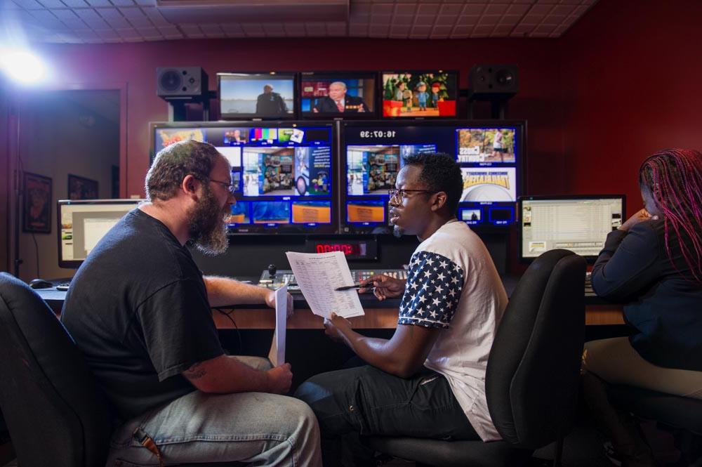 A student working with their professor next to broadcasting equipment