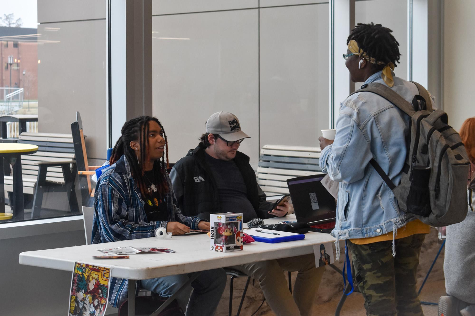 Students sitting at a table inside Jefferson Student Union and talking to another student