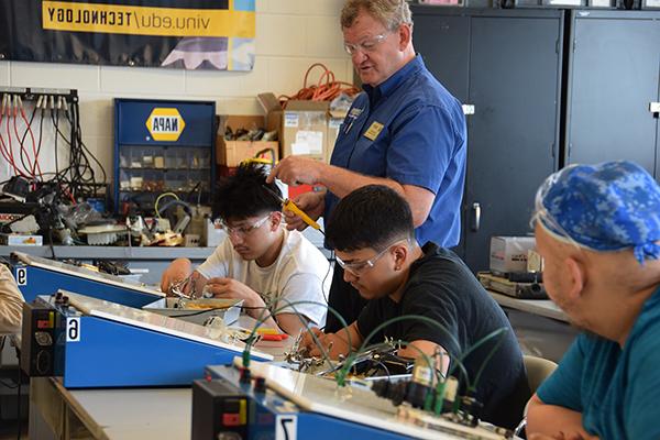 An engineering professor observing his students connecting wires to boards